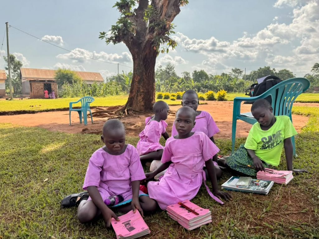 Students sitting beneath a tree with books, notebooks, and school supplies