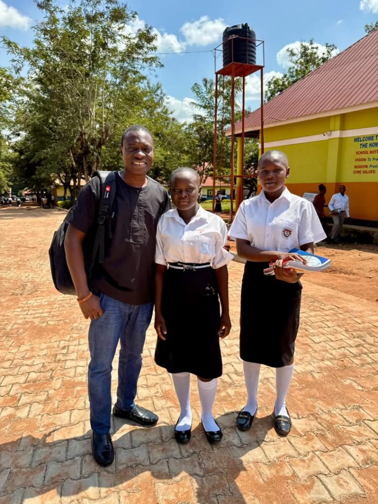 Foundation representative standing with two students in school uniforms holding books