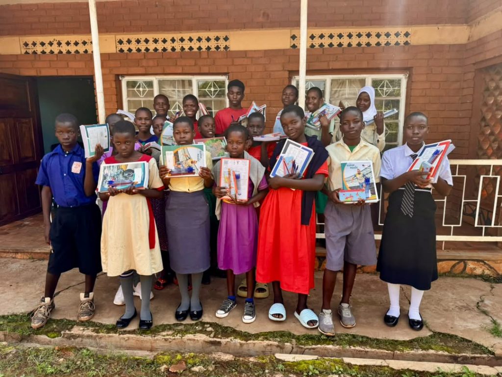 Group of students standing together while holding books, notebooks, and pens
