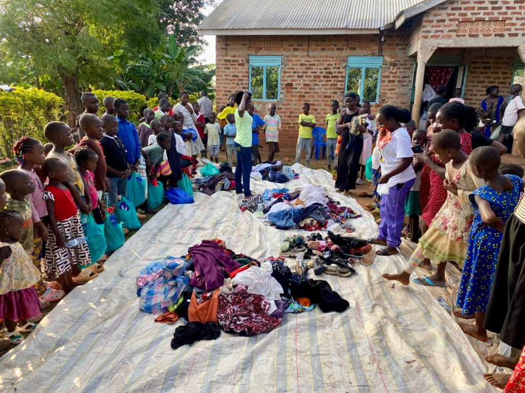 Children and adults gathered around clothing and shoes displayed on a large ground covering