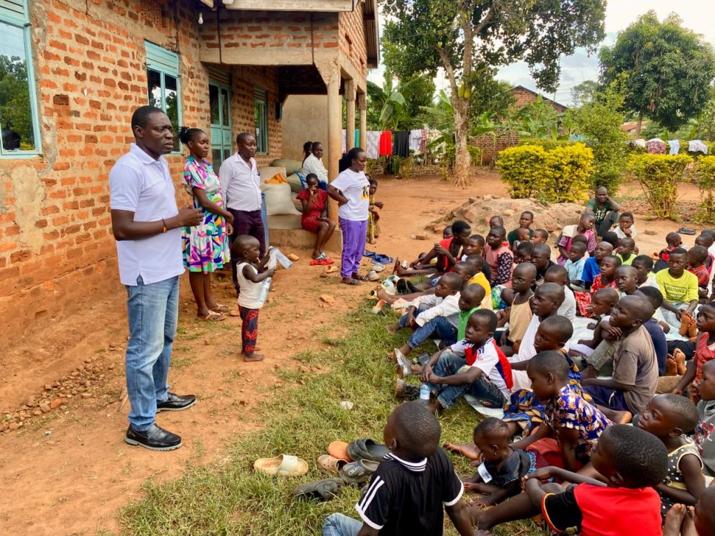 Johns Brown speaking to a large group of children seated outside in Kamuli District